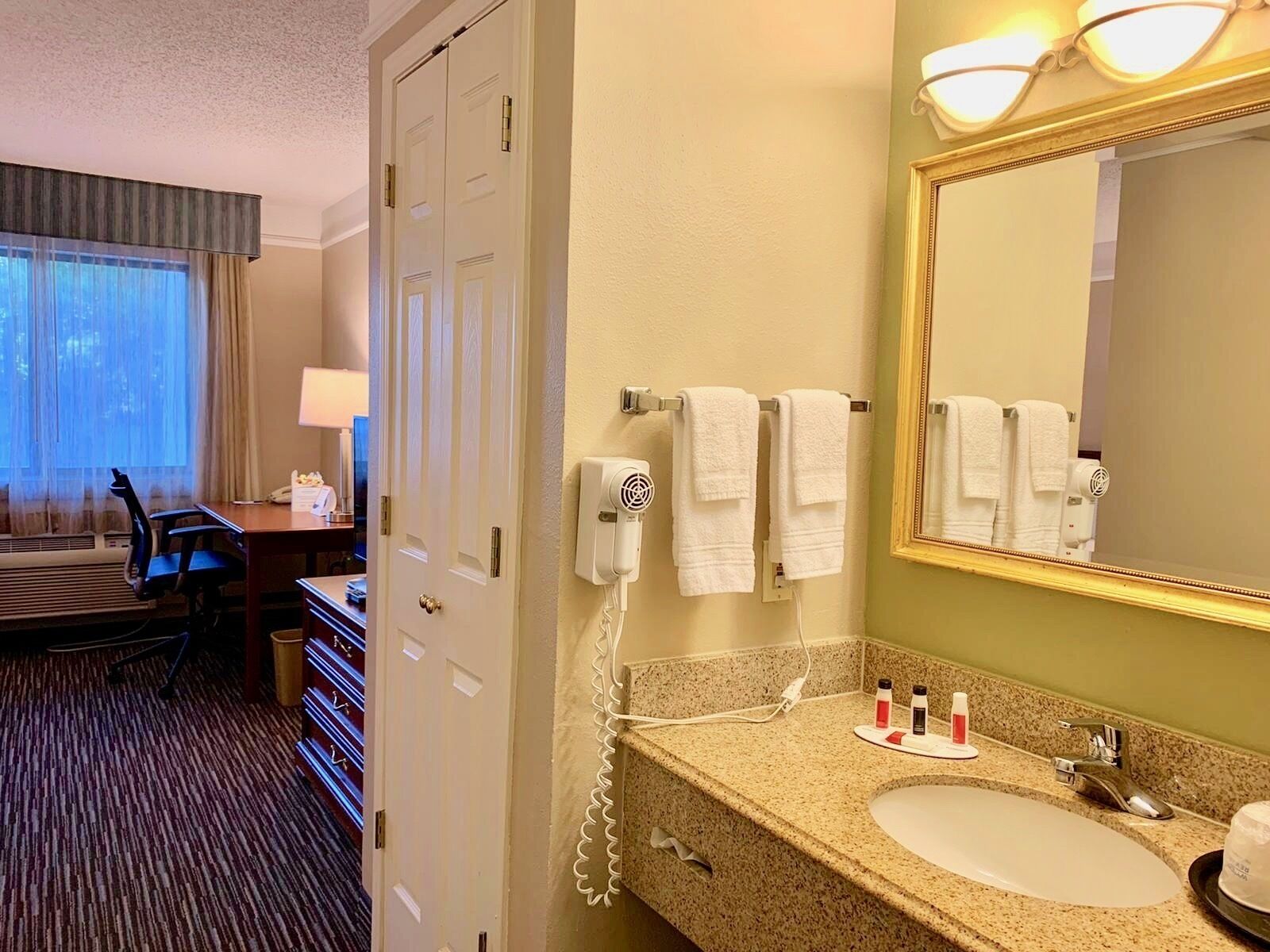 Un baño de hotel con lavamanos, espejo, toallero y secador de pelo.