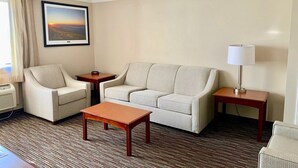 A hotel room with a sofa, armchair, small table, lamp, and a framed picture on the wall. - Baymont by Wyndham Texarkana (Texarkana)