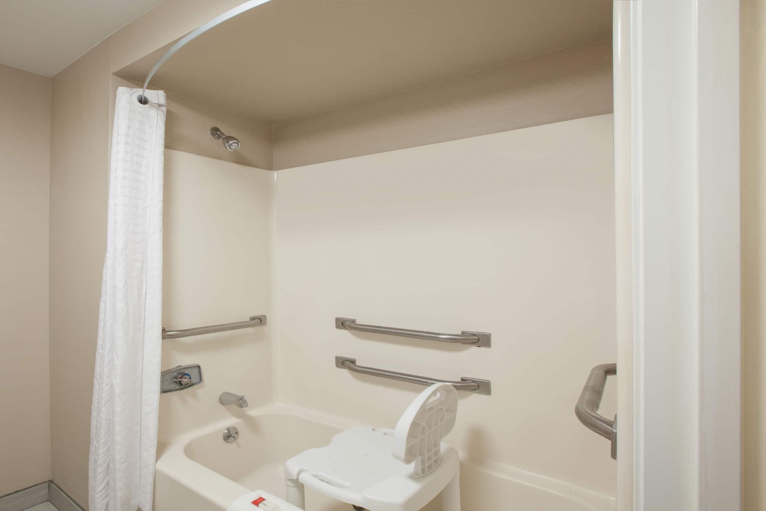 A shower with a white curtain, a handheld showerhead, and a grab bar.