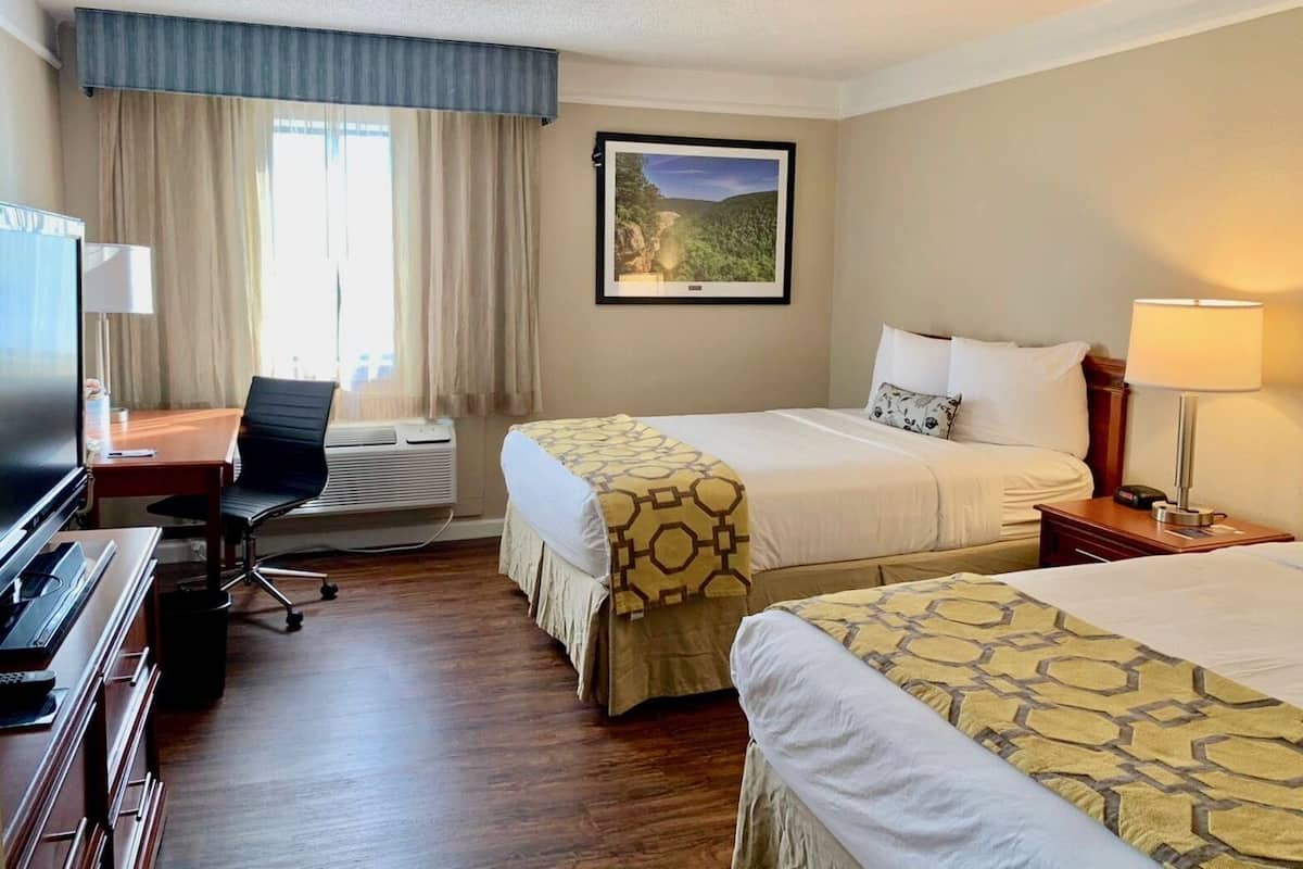 Habitación de hotel con dos camas, un escritorio con silla, televisión y ventana con cortinas.