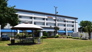 A modern hotel with a flat roof, a covered outdoor seating area, and a swimming pool in the background. - Baymont by Wyndham Texarkana (Texarkana)