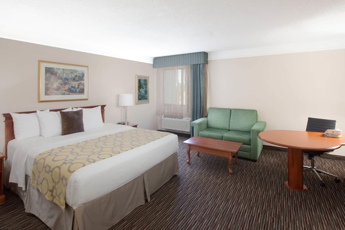Una habitación de hotel con una cama, un sillón verde, una mesita, una lámpara y un cuadro en la pared.