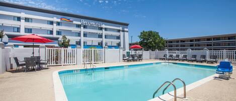 A swimming pool with lounge chairs and umbrellas, a building with a 'Baymont' sign, and a clear blue sky.