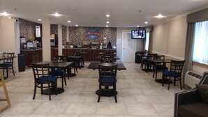 A breakfast area with tables and chairs, a kitchen in the background, and a TV on the wall. - Baymont by Wyndham Texarkana (Texarkana)