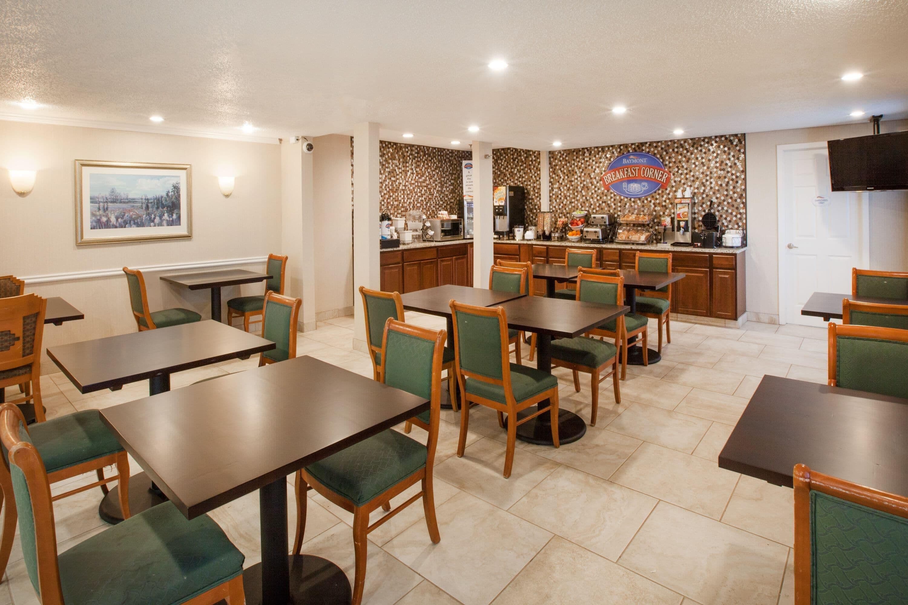 A dining area with multiple tables and chairs, a kitchen area with a coffee machine, and a framed picture on the wall.