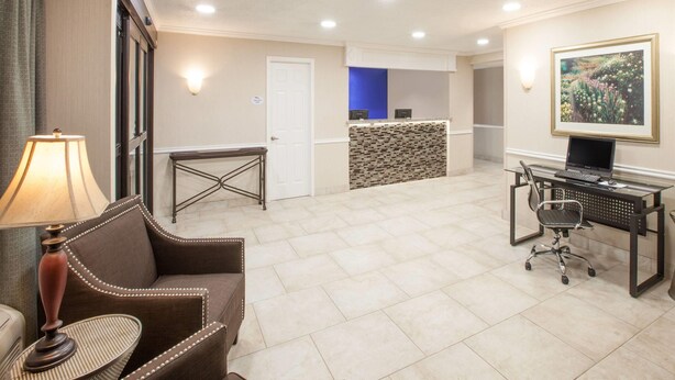 A hotel room with a sofa, a small table, a desk with a computer, a lamp, and a painting on the wall. - Baymont by Wyndham Texarkana (Texarkana)