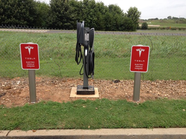 A Tesla electric vehicle charging station with two signs, a grassy area, and a fence in the background. - Super 8 by Wyndham Russellville (Russellville)