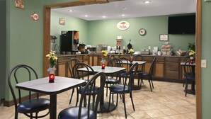 A breakfast restaurant with tables and chairs, a kitchen area, and a clock on the wall. - Super 8 by Wyndham Russellville (Russellville)