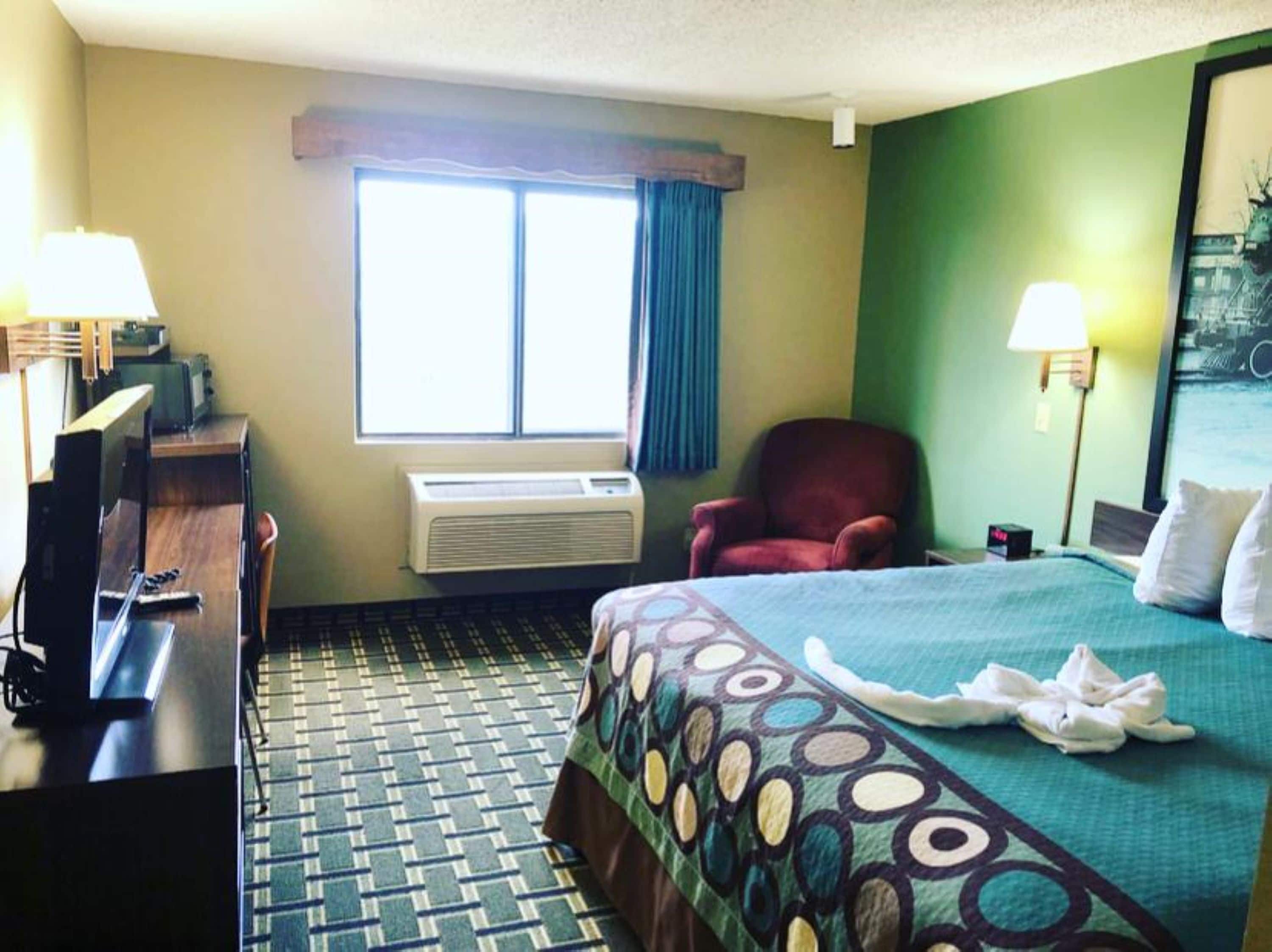 Habitación de hotel con cama, escritorio, silla, aire acondicionado y ventana con cortinas.