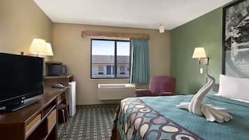 A hotel room with a bed, a desk with a television, a chair, a window with curtains, and a wall-mounted air conditioner.