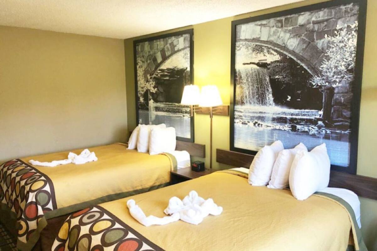 A hotel room with two beds, each with a yellow bedspread and white pillows, a nightstand with a lamp, and a large framed picture of a waterfall.