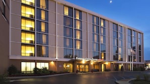 A multi-story hotel with a large entrance, a parking lot, and a well-lit facade.