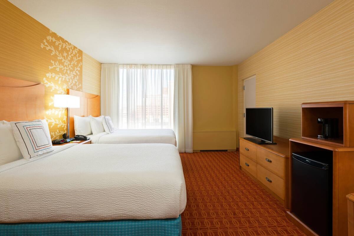 A hotel room with two beds, a television, a coffee machine, and a desk with drawers.