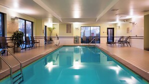An indoor swimming pool with clear water, surrounded by lounge chairs and a potted plant.