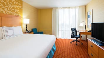 Ein Hotelzimmer mit einem großen Bett, einem Schreibtisch mit Stuhl, einem Fernseher und einem Fenster mit Vorhängen.