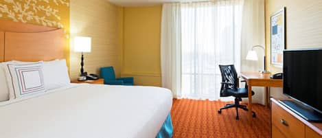 A hotel room with a large bed, a desk with a chair, a television, and a window with curtains.