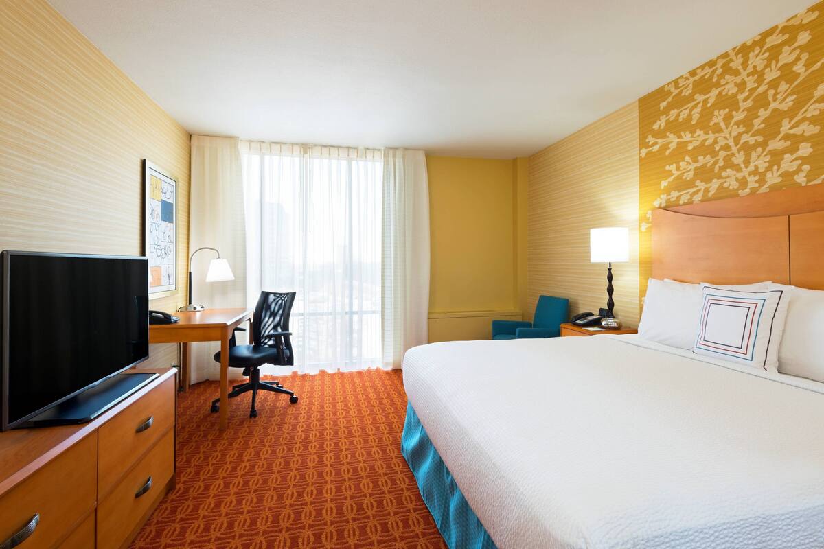A hotel room with a bed, a desk with a chair, a television, and a lamp.