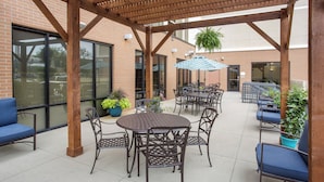 An outdoor patio with a pergola, tables, chairs, and potted plants.
