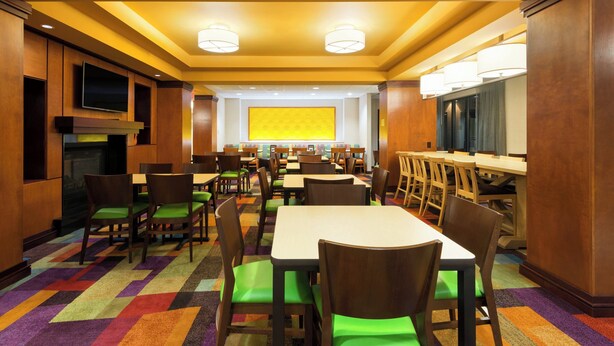 A hotel dining area with multiple tables and chairs, a large screen, and a patterned carpet.