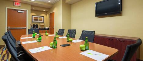 A conference room with a long table, chairs, a TV mounted on the wall, and an exit sign.