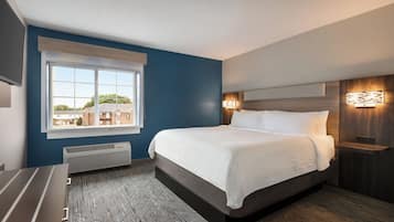 Una habitación de hotel moderna con una cama grande, una ventana con persianas, un calentador integrado y una mesita de noche con lámpara.