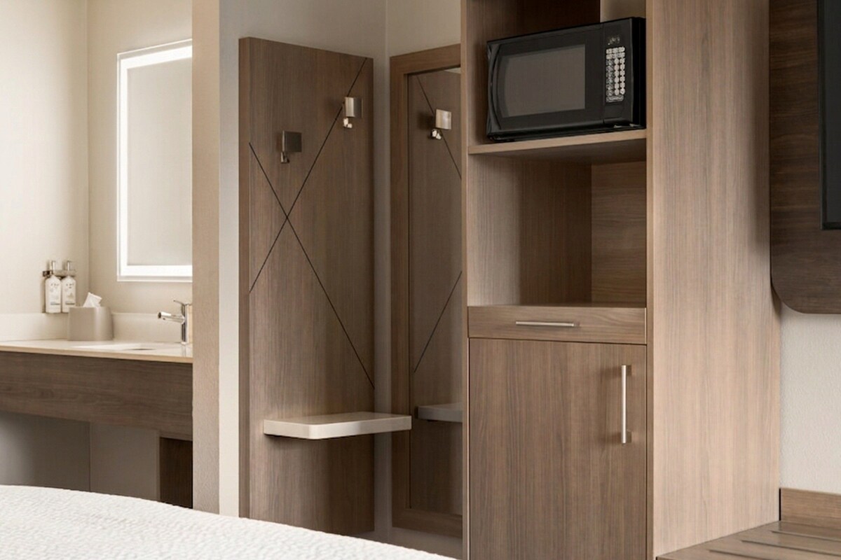 Een moderne badkamer met een houten wastafelmeubel, een spiegel en een magnetron.