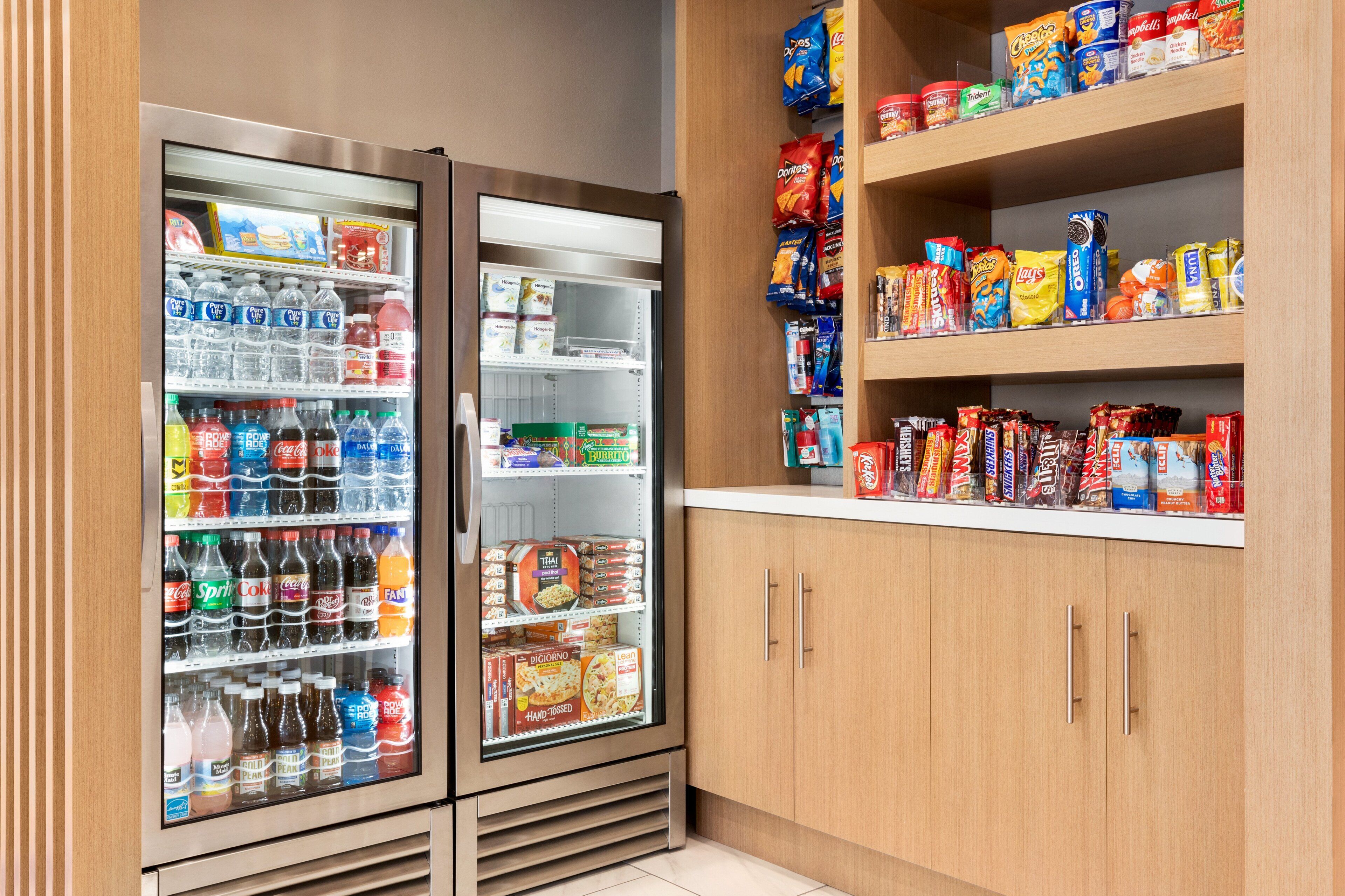 A self-service beverage and snack area with refrigerated drinks and a variety of snacks on shelves.