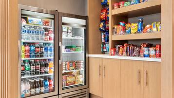 A self-service beverage and snack area with refrigerated drinks and a variety of snacks on shelves.