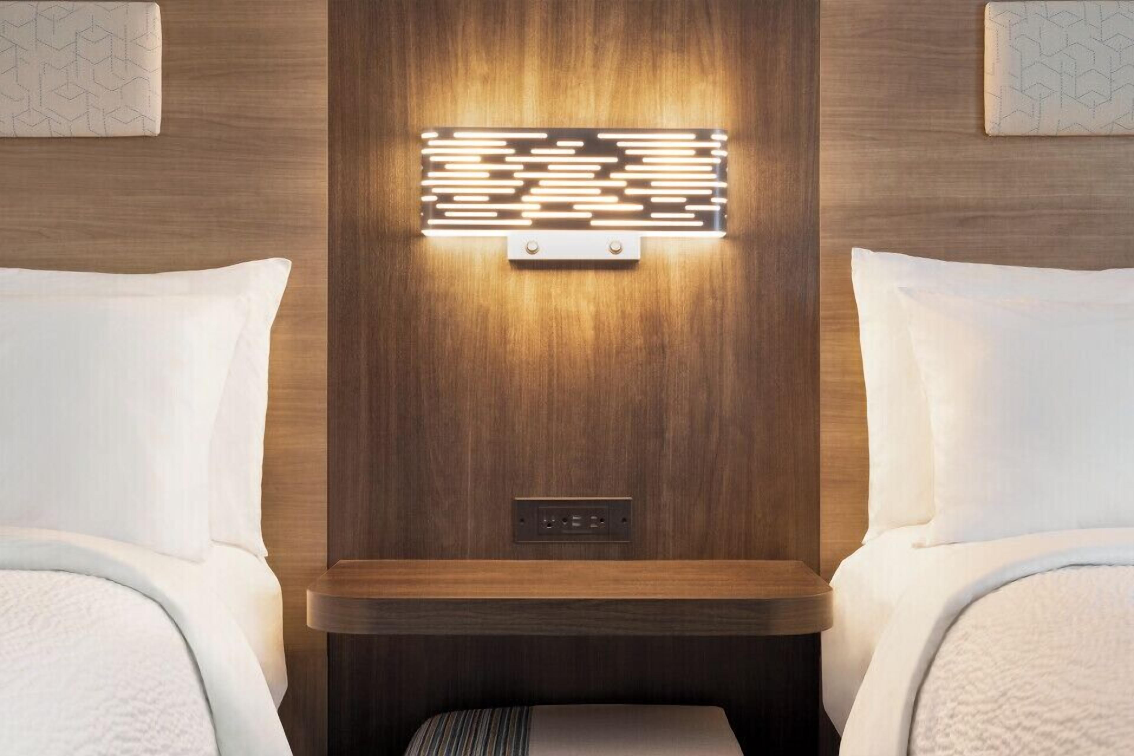 Una habitación de hotel con cabecera de madera, una mesita de noche y un aplique de pared.