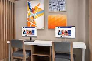 Un espacio de oficina moderno con dos monitores de computadora sobre un escritorio blanco, dos sillas grises y una obra de arte abstracta en la pared.