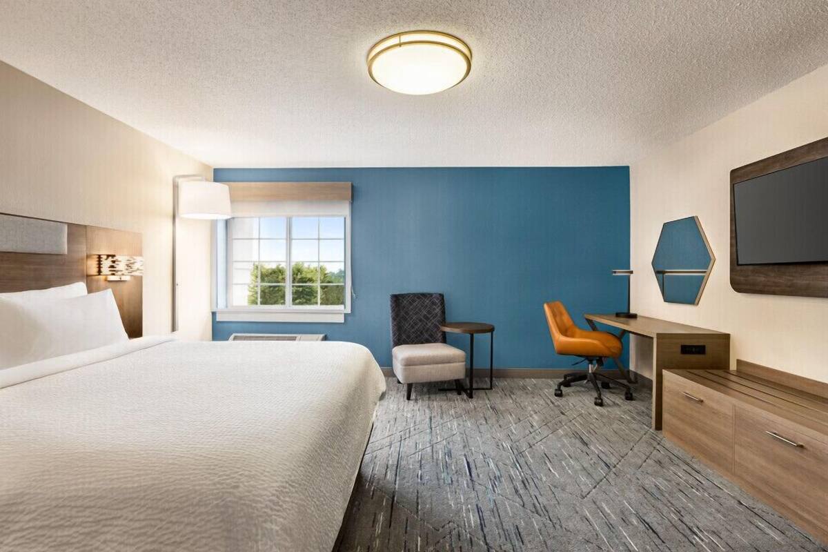 A hotel room with a large bed, a desk, a chair, and a TV on the wall.
