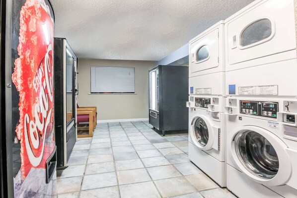 A laundry room with stacked washers and dryers, a refrigerator, and a Coca-Cola vending machine.
