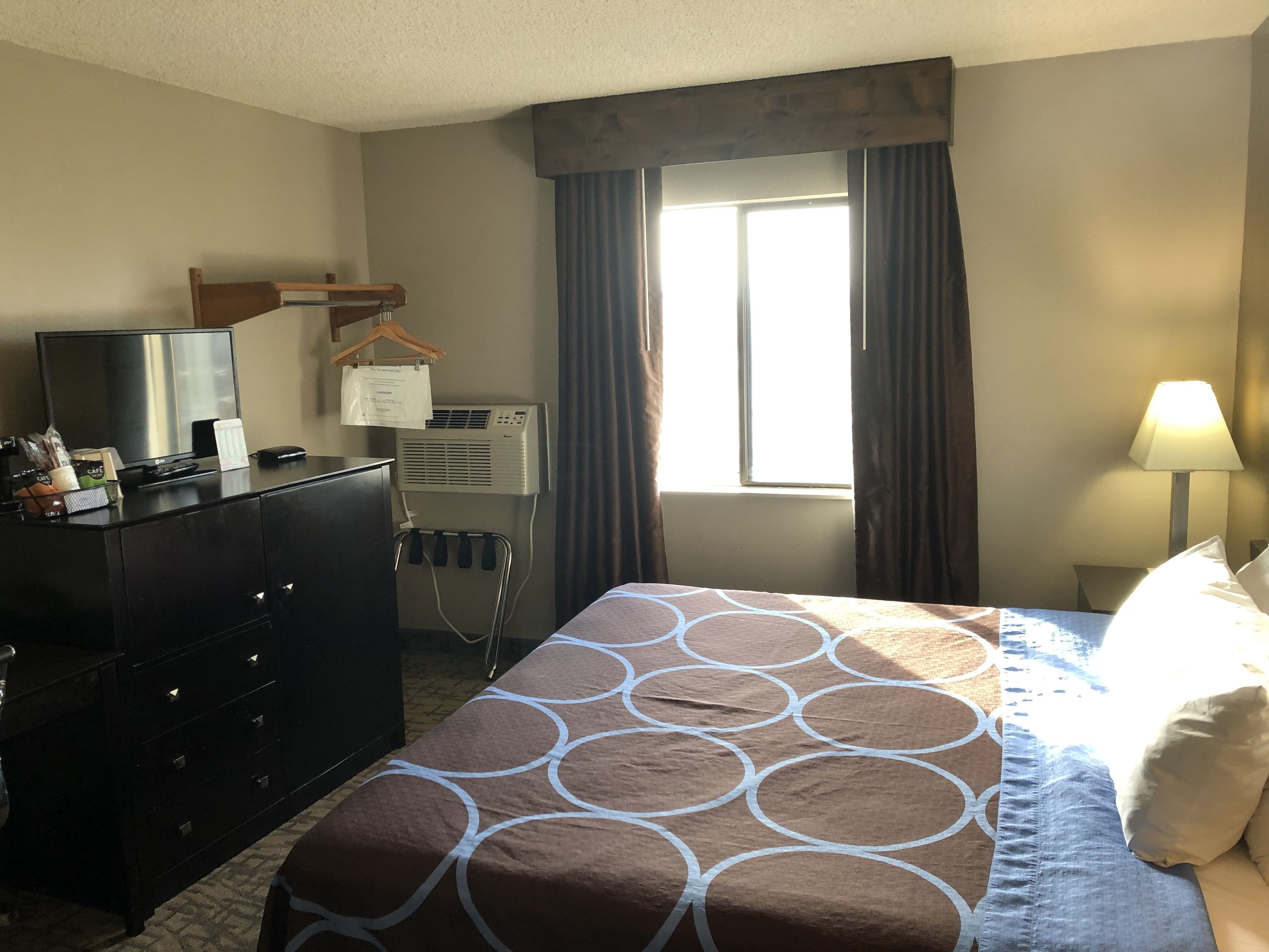 Une chambre d’hôtel équipée d’un lit, d’une commode, d’une télévision, d’un climatiseur et d’une fenêtre avec des rideaux.