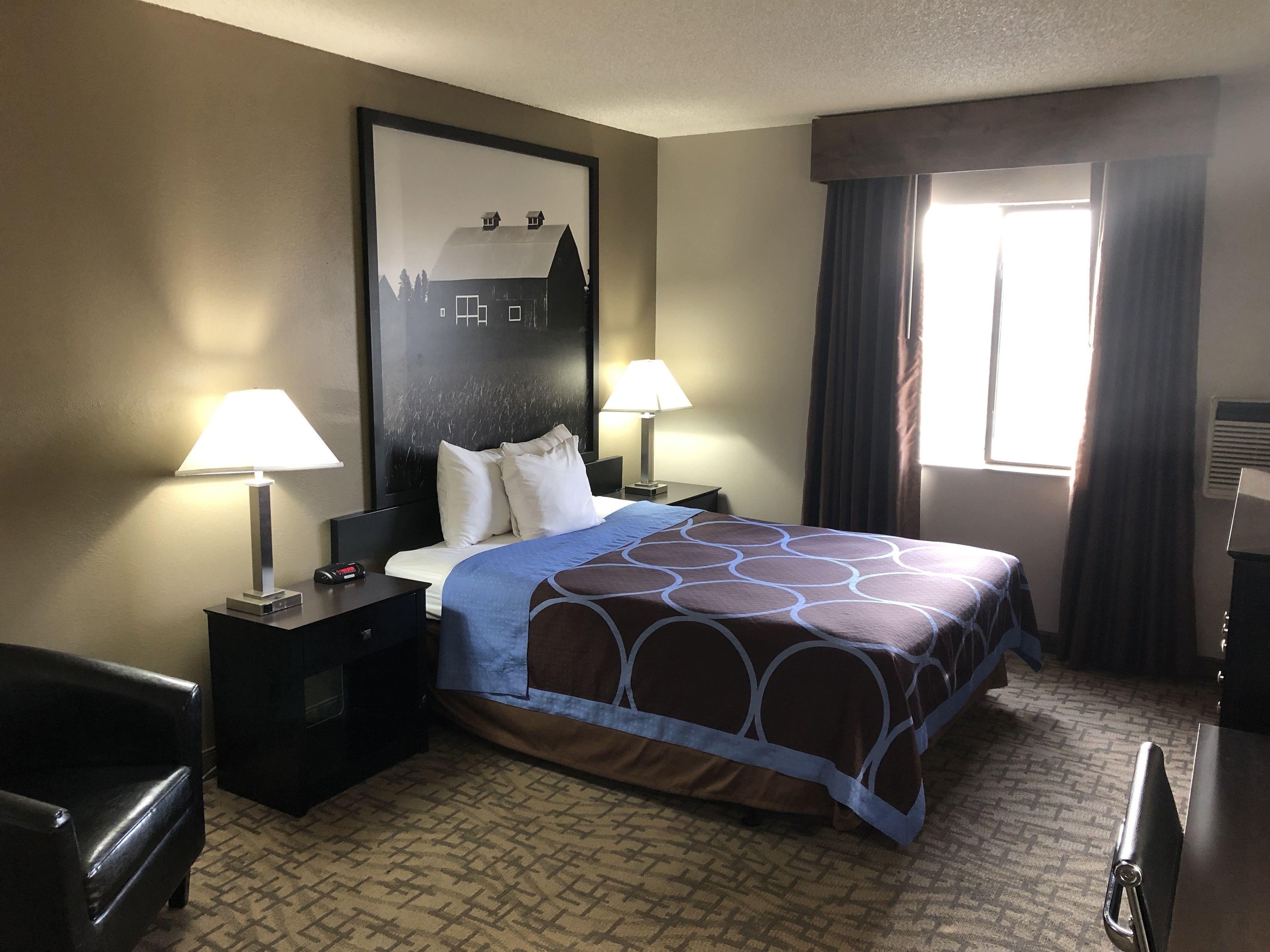 Habitación de hotel con una cama grande, dos lámparas de noche, una mesita de noche, una silla y una ventana con cortinas.
