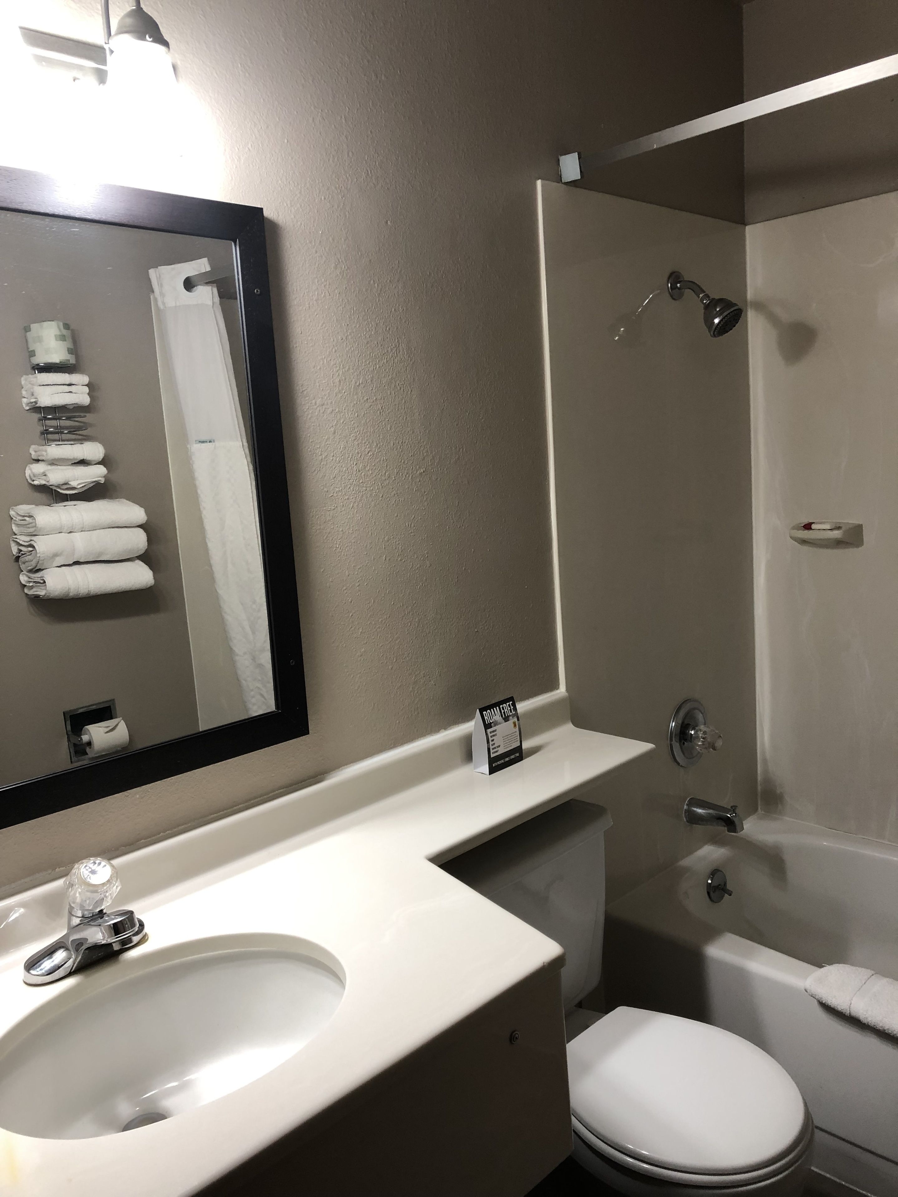 A bathroom with a sink, toilet, and shower. There is a towel rack with towels, a mirror, and a sign indicating the room is free.