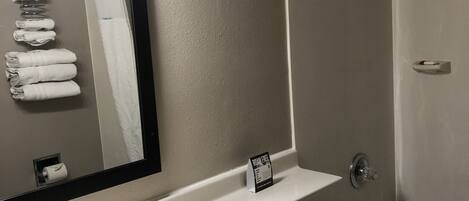 A bathroom with a sink, toilet, and shower. There is a towel rack with towels, a mirror, and a sign indicating the room is free.