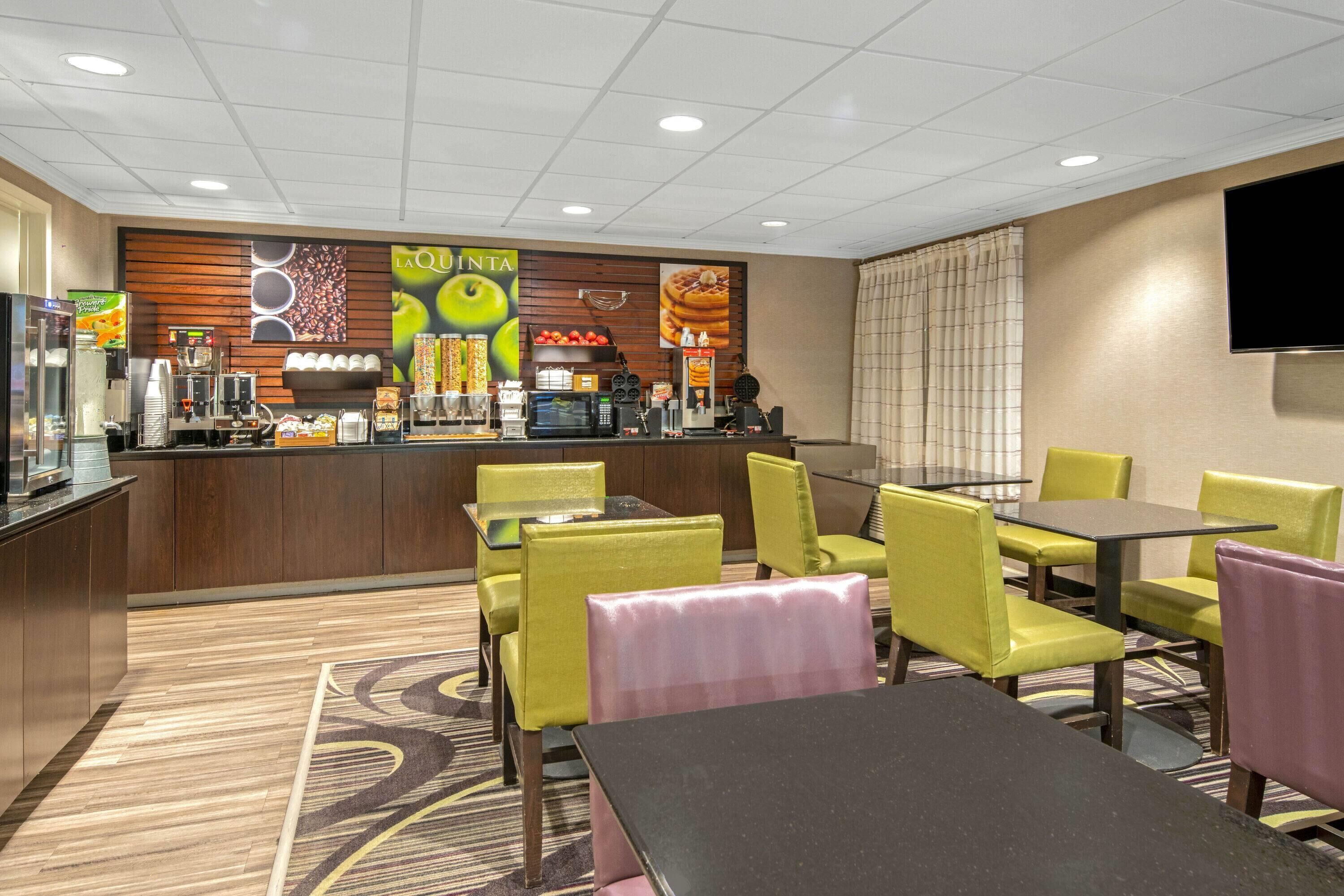 A restaurant with a counter, chairs, tables, and a TV mounted on the wall.