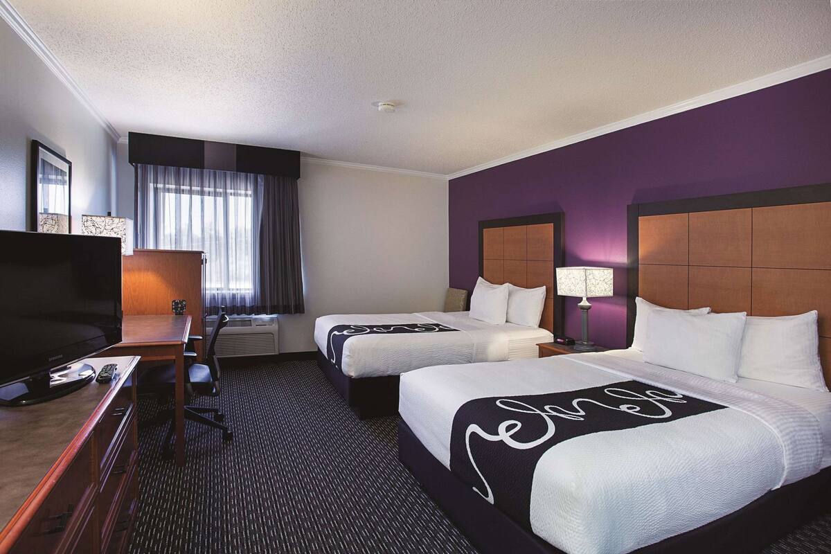 A hotel room with two beds, a television, a desk, and a chair.