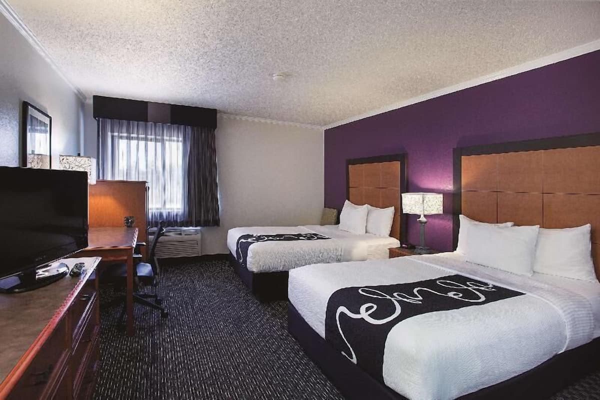 A hotel room with two beds, a desk with a TV, and a window with curtains.