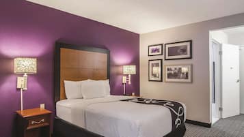 Quarto de hotel com cama, mesa de cabeceira, luminárias fixadas na parede e quadros emoldurados.