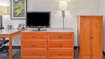 A hotel room with a flat-screen TV, a wooden cabinet, a desk with a telephone, and a framed picture on the wall.