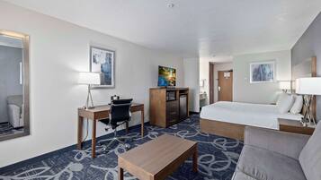 A hotel room with a bed, a desk with a chair, a small table, a sofa, and a TV.