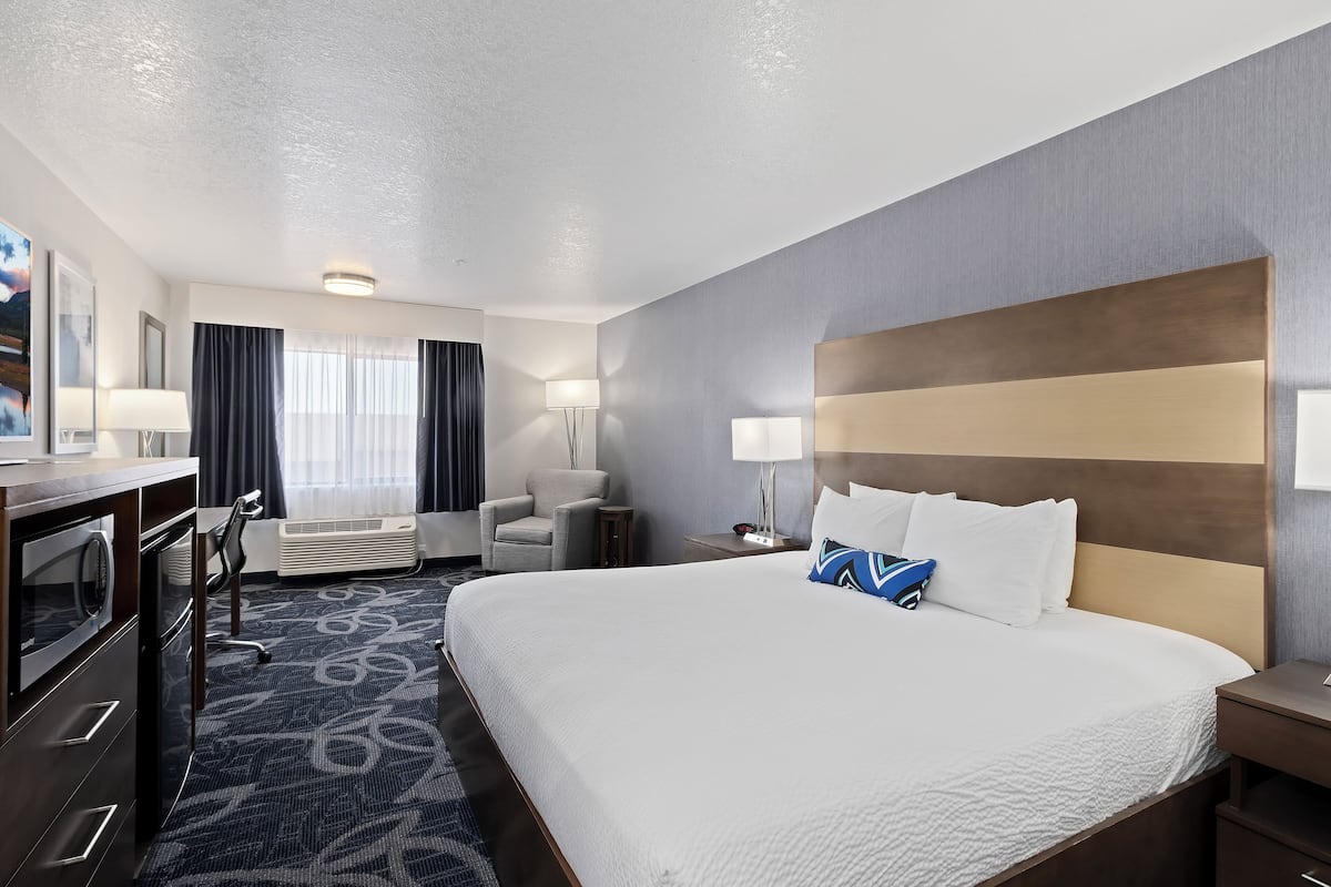 A hotel room with a large bed, a desk, a chair, and a lamp.