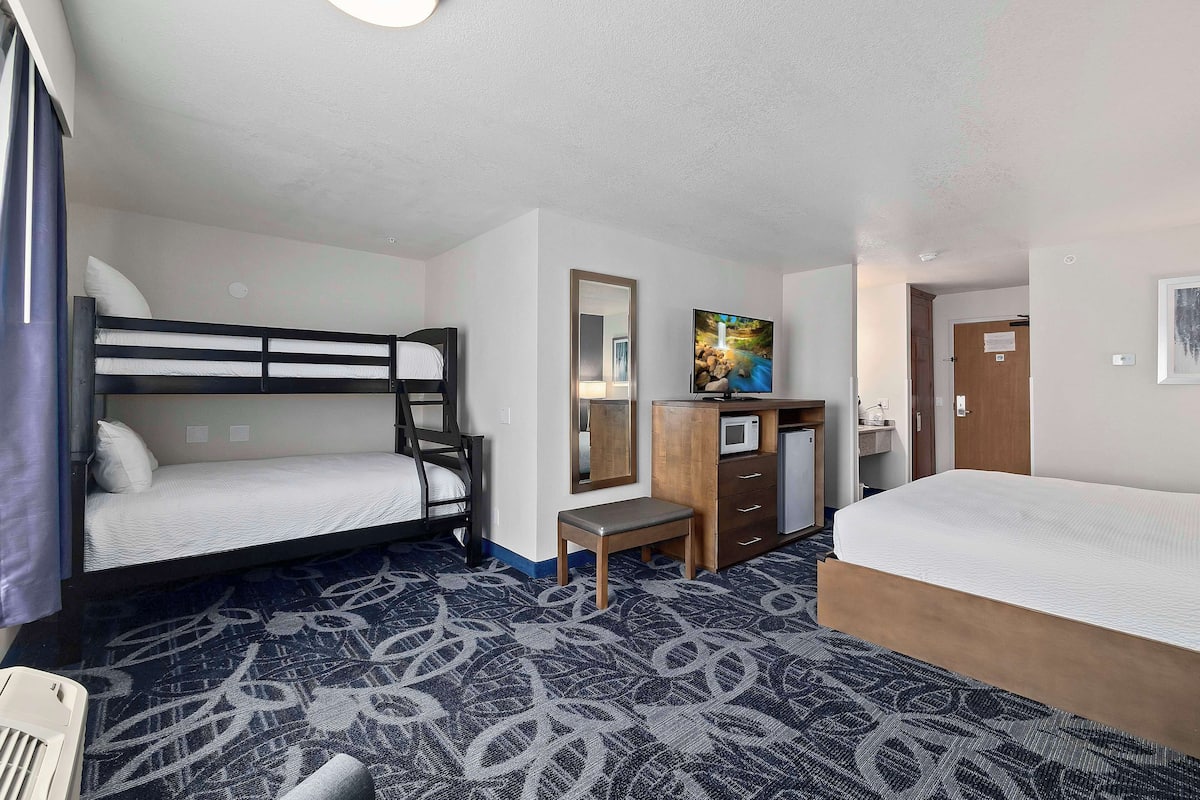 A hotel room with a bunk bed, a desk with a chair, a small table, and a bed.