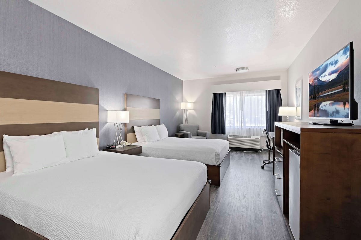 A hotel room with two beds, a desk, a chair, a TV, and a window with curtains.
