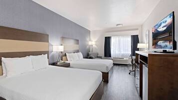 Une chambre d’hôtel avec deux lits, un bureau, une chaise, une télévision et une fenêtre avec des rideaux.