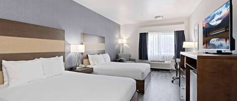 A hotel room with two beds, a desk, a chair, a TV, and a window with curtains.