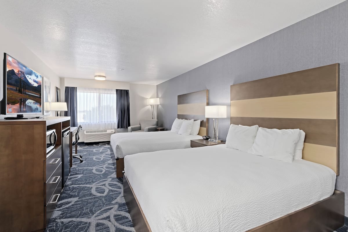 A hotel room with two beds, a desk, a chair, and a TV.