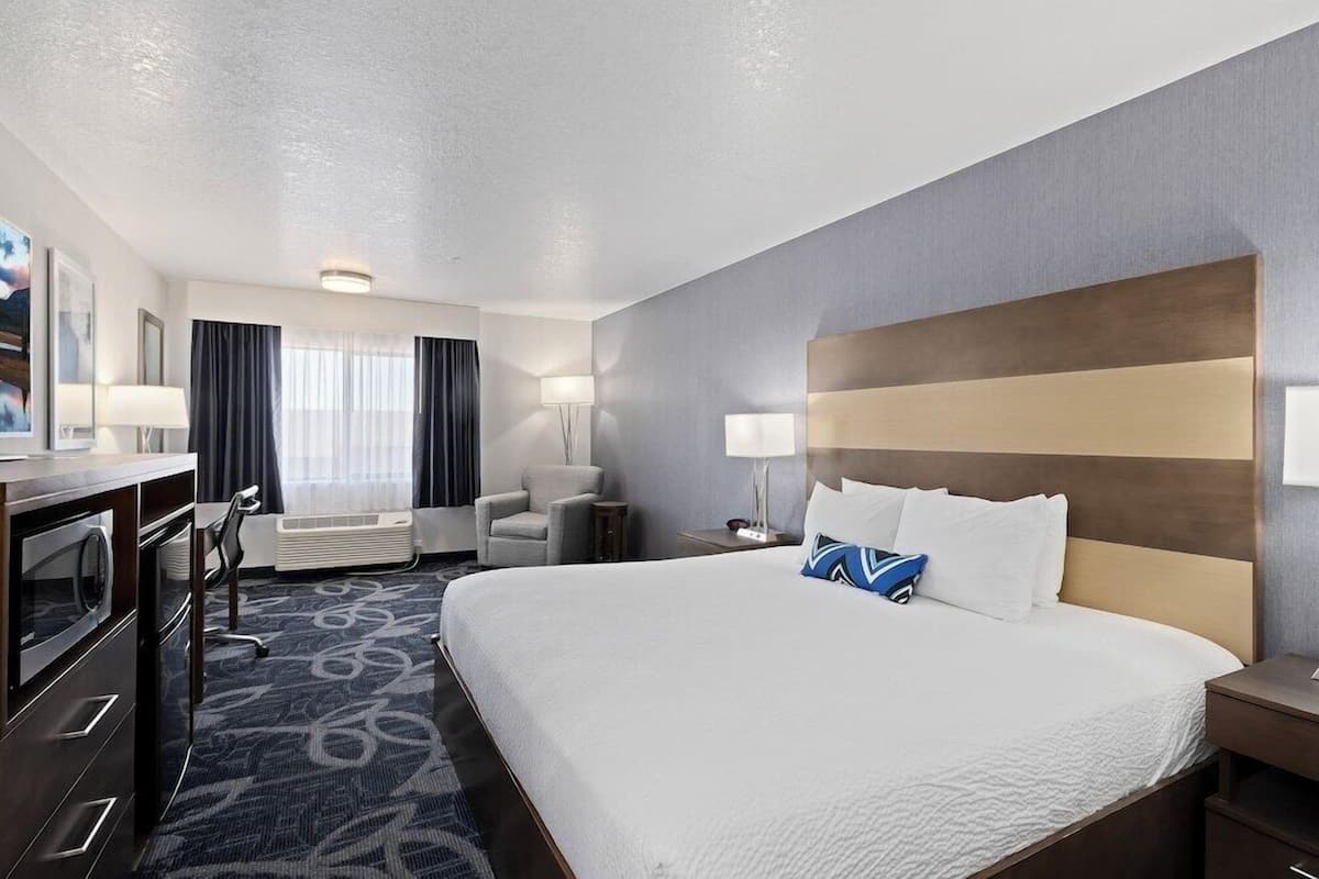 A hotel room with a large bed, a desk, a chair, and a small table.