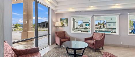 A modern hotel lobby with large windows, comfortable seating, and a view of the pool.